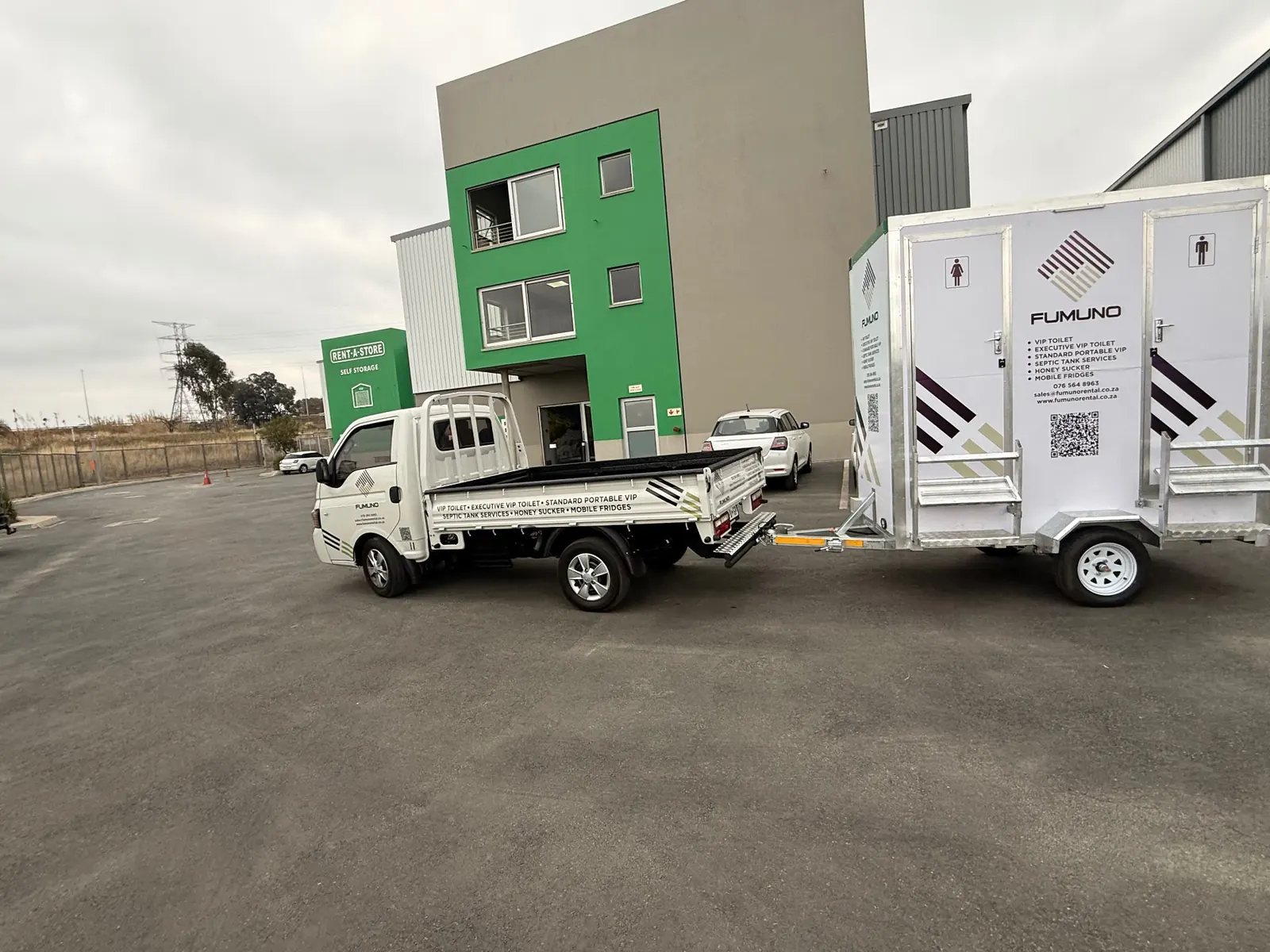 Fumuno bakkie hitched to a branded twin-door VIP mobile toilet trailer with male and female doors and galvanised steps, ready to leave the Fumuno depot in Gauteng